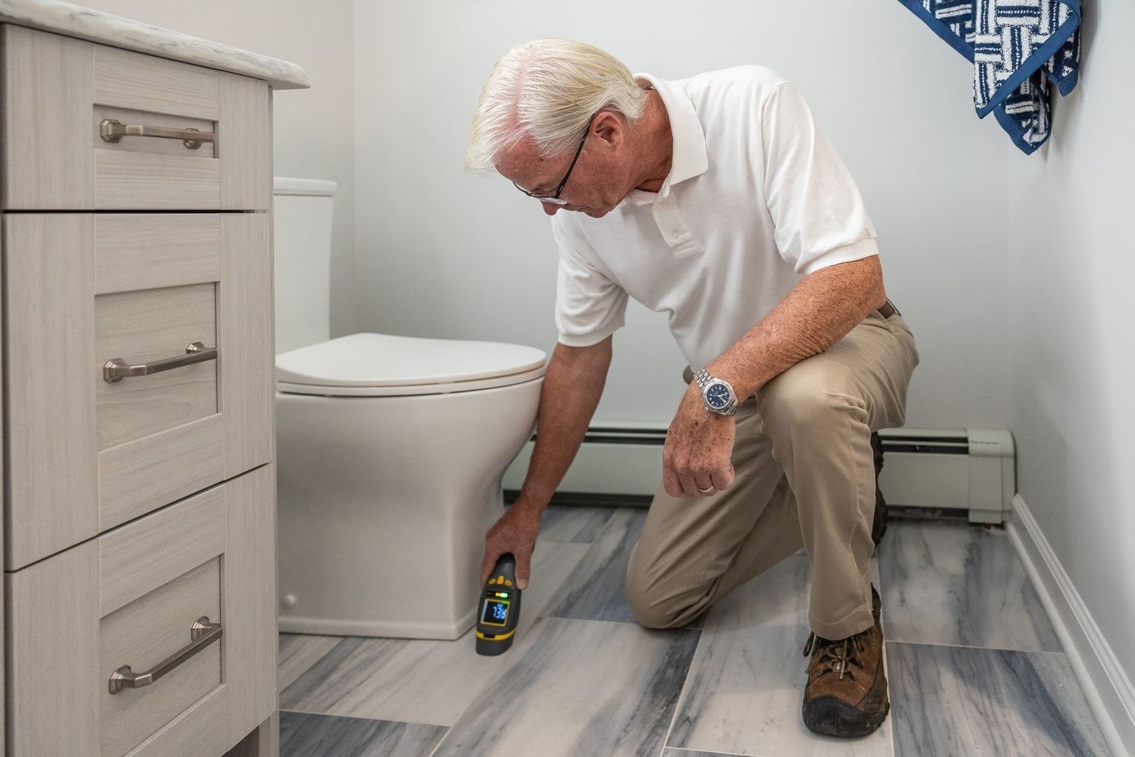 Oudere man inspecteert de vloer in een badkamer met een meetapparaat